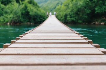 Obraz premium A wooden suspension bridge stretches over a river, surrounded by lush green trees, fading into the distance.