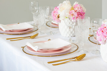 Elegant wedding table setting with pink peonies, gold cutlery, and crystal glassware, creating a romantic and sophisticated atmosphere.