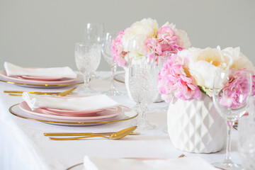 Elegant wedding table setting with pink peonies, gold cutlery, and crystal glassware, creating a romantic and sophisticated atmosphere.