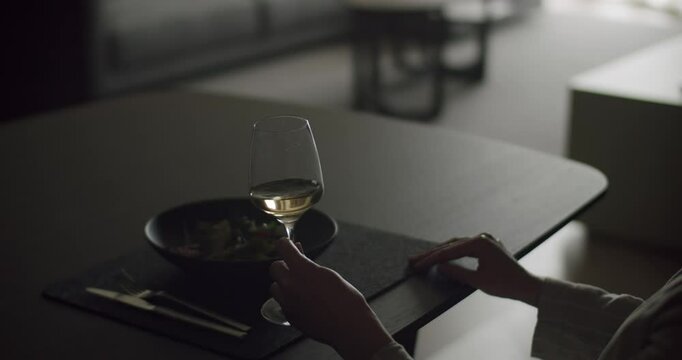 A serene image of a person holding a glass of white wine while dining in a cozy, dimly lit setting. The setting exudes relaxation and sophistication, perfect for a quiet evening meal. Glass of Wine
