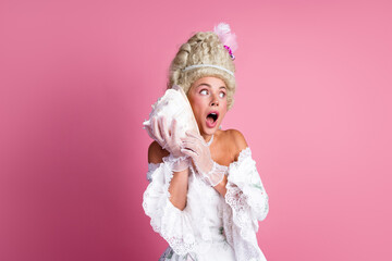 Young woman dressed in an elegant baroque costume holding a seashell against pastel backdrop portraying a whimsical scene