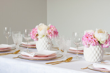 Elegant wedding table setting with pink peonies, gold cutlery, and crystal glassware, creating a romantic and sophisticated atmosphere.