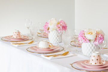 Elegant wedding table setting with pink peonies, gold cutlery, and crystal glassware, creating a romantic and sophisticated atmosphere.