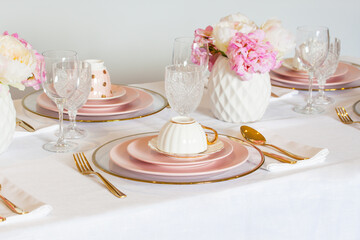 Elegant wedding table setting with pink peonies, gold cutlery, and crystal glassware, creating a romantic and sophisticated atmosphere.
