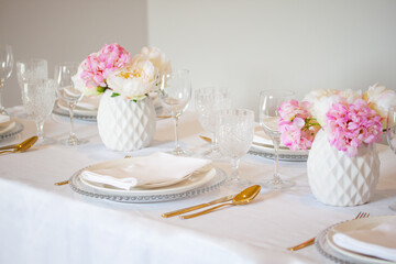 Elegant wedding table setting with pink peonies, gold cutlery, and crystal glassware, creating a romantic and sophisticated atmosphere.
