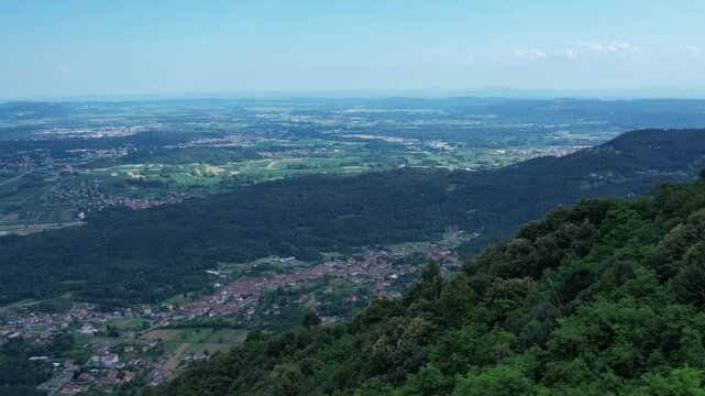 Drone panorama of the Ivrea Morainic Amphitheatre seen from Brosso, Val Chiusella, Italy, showing lush green plains, woods, and scattered villages under clear sky, high drone shot, slow motion