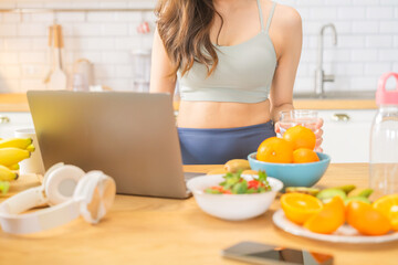 fit Asian female in sportswear enjoys a colorful fruit shake and fresh mineral water while unwinding at home in the early hours, embracing a mindful lifestyle and remote work wellness routine