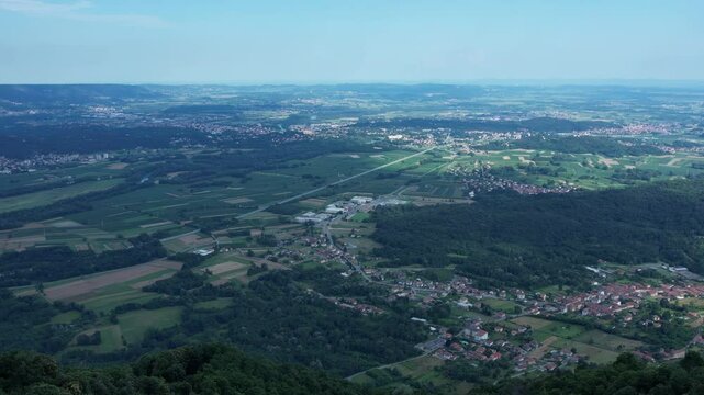 Drone panorama of the Ivrea Morainic Amphitheatre seen from Brosso, Val Chiusella, Italy, showing lush green plains, woods, and scattered villages under clear sky, high drone shot, slow motion