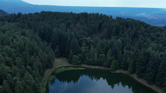 low motion drone view of Meugliano Lake bordered by dense conifer woods in Val di Chy, part of the Ivrea Morainic Amphitheatre, a prehistoric glacial landform in northern Piedmont, drone shot