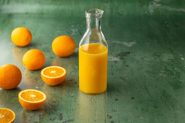 Freshly squeezed orange juice in glass bottle surrounded by oranges on green rustic wooden table