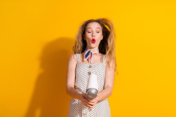 Young woman with stylish hair enjoys summer fun holding a dryer against vivid yellow backdrop...