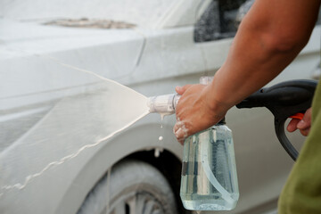 Man washing car with soap and water, creating bubbles and foam; outdoor car wash service focused on...