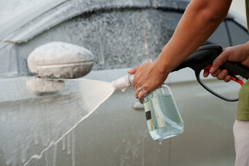 Man washing car with soap and water, creating bubbles and foam; outdoor car wash service focused on...