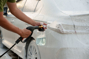 Man washing car with soap and water, creating bubbles and foam; outdoor car wash service focused on...