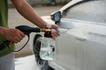 Man washing car with soap and water, creating bubbles and foam; outdoor car wash service focused on...