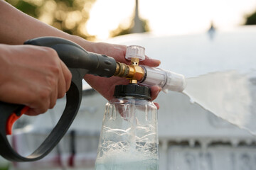 Man washing car with soap and water, creating bubbles and foam; outdoor car wash service focused on...