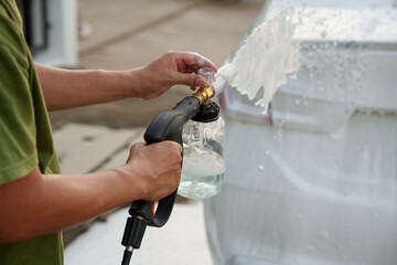 Man washing car with soap and water, creating bubbles and foam; outdoor car wash service focused on...