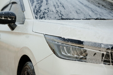 Man washing car with soap and water, creating bubbles and foam; outdoor car wash service focused on...