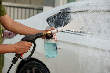 Man washing car with soap and water, creating bubbles and foam; outdoor car wash service focused on...