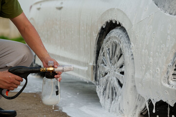 Man washing car with soap and water, creating bubbles and foam; outdoor car wash service focused on...