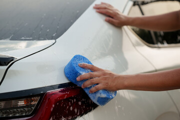 Man washing car with soap and water, creating bubbles and foam; outdoor car wash service focused on...