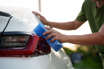 Man washing car with soap and water, creating bubbles and foam; outdoor car wash service focused on...