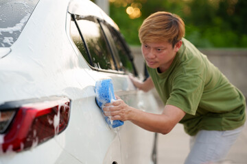 Man washing car with soap and water, creating bubbles and foam; outdoor car wash service focused on...