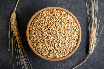 Wheat grains in wooden bowl and ears on top view