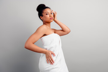 Fototapeta premium Elegant young woman wrapped in a towel posing with confidence on a neutral background emphasizing beauty and self-care