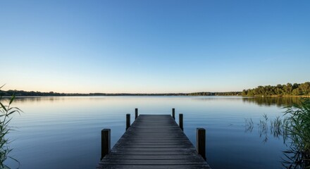 Fototapeta premium Calm wooden pier extending into a serene lake at dawn