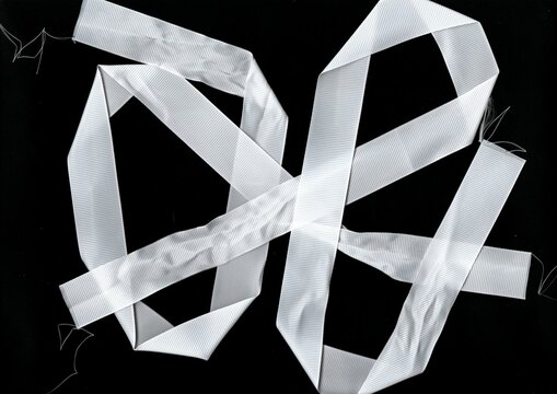 White satin ribbons twisted in loops on black background. High-contrast scan showing glossy surface and delicate fabric.