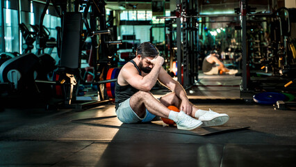 Tired man sitting on gym floor with head down after intense workout with medicine ball, symbolizing...