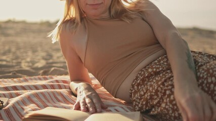 Blonde woman reading book, reclining on striped towel, basking in sunlight during beach getaway, radiating calm and relaxation.Summer concept.Lifestyle, vacation, tourism,nature, active life - Powered by Adobe