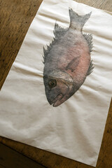 Detailed Gyotaku fish print on rice paper, with visible ink textures and imperfections, placed on a wooden table surface.