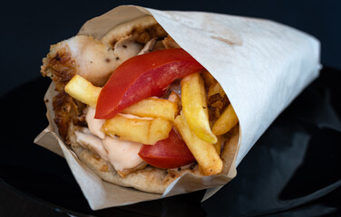 Photo of a delicious Greek gyros sandwich wrap with chicken tomato and sauce.	
