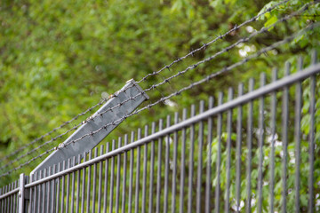 Gray iron fence topped with angled barbed wire, symbolizing security, protection, and restricted...