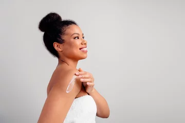  Young woman with radiant skin applying lotion on her shoulder, highlighting beauty and skincare routines © deagreez