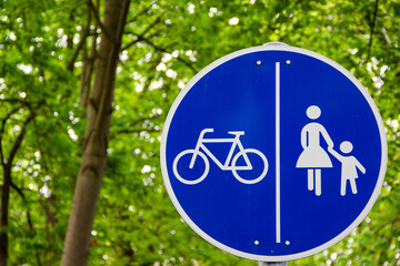 Round blue road sign with bicycle and woman with child separated by a vertical line. Pedestrian and...