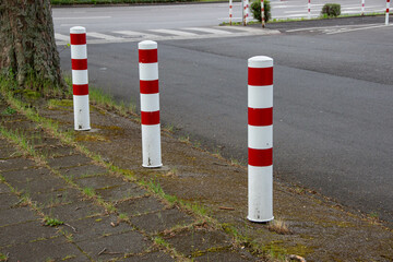 Three white bollards with red stripes blocking the sidewalk, separating pedestrians from cars for safety. Urban traffic safety concept.