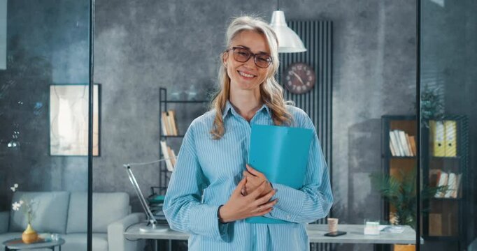 Portrait of a female businesswoman in leadership standing in a modern office and looking at the camera with a smile, holding a folder in her hands.