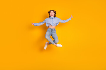 Obraz premium Joyful young girl jumping against vibrant yellow background in casual outfit, expressing happiness and energetic emotions