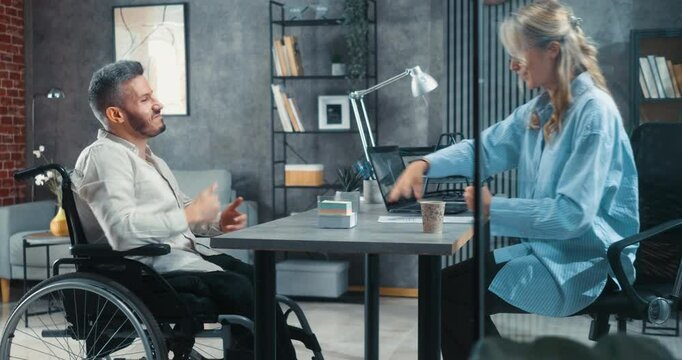 A satisfied man with disability in a wheelchair signs an employment contract after a successful job interview with a female employer in a modern office.