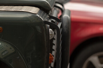The image shows a closeup of a vehicles grill, highlighting its intricate metal parts and design, with a partially visible red car in the background for added composition