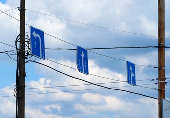Three Road signs of the direction of movement along the lanes, hanging over a road between poles...
