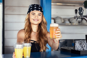 Hipster bartender girl serving beer and fresh lemonade at outdoor summer festival bar
