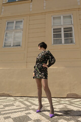 In a vibrant city, a model flaunts a floral dress and purple heels by a modern building, showcasing...