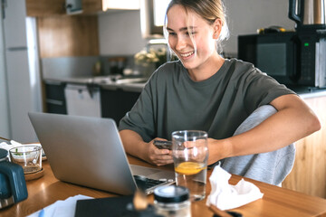  Gen Z woman working from home at cozy kitchen table with laptop and phone. Digital nomad lifestyle, mindfulness, remote work, balance, mental calm and modern freelancing