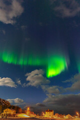 Equinox Aurora Borealis over illuminated house, island of Hillesøya with dancing northern lights clear colored rays of light, green light in the sky with red and purple strikes! amazing joy in Norway