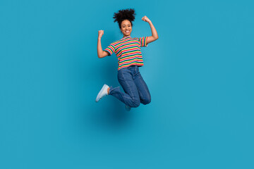 Energetic young woman jumping joyfully in casual striped t-shirt and jeans on a bright turquoise...