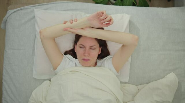 Young adult woman lies in bed in the morning and rubs her hand, who is numb after sleeping in an uncomfortable position